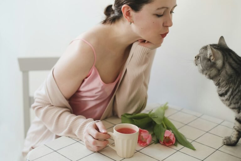 a person sitting on a chair with a cat and a cup of tea