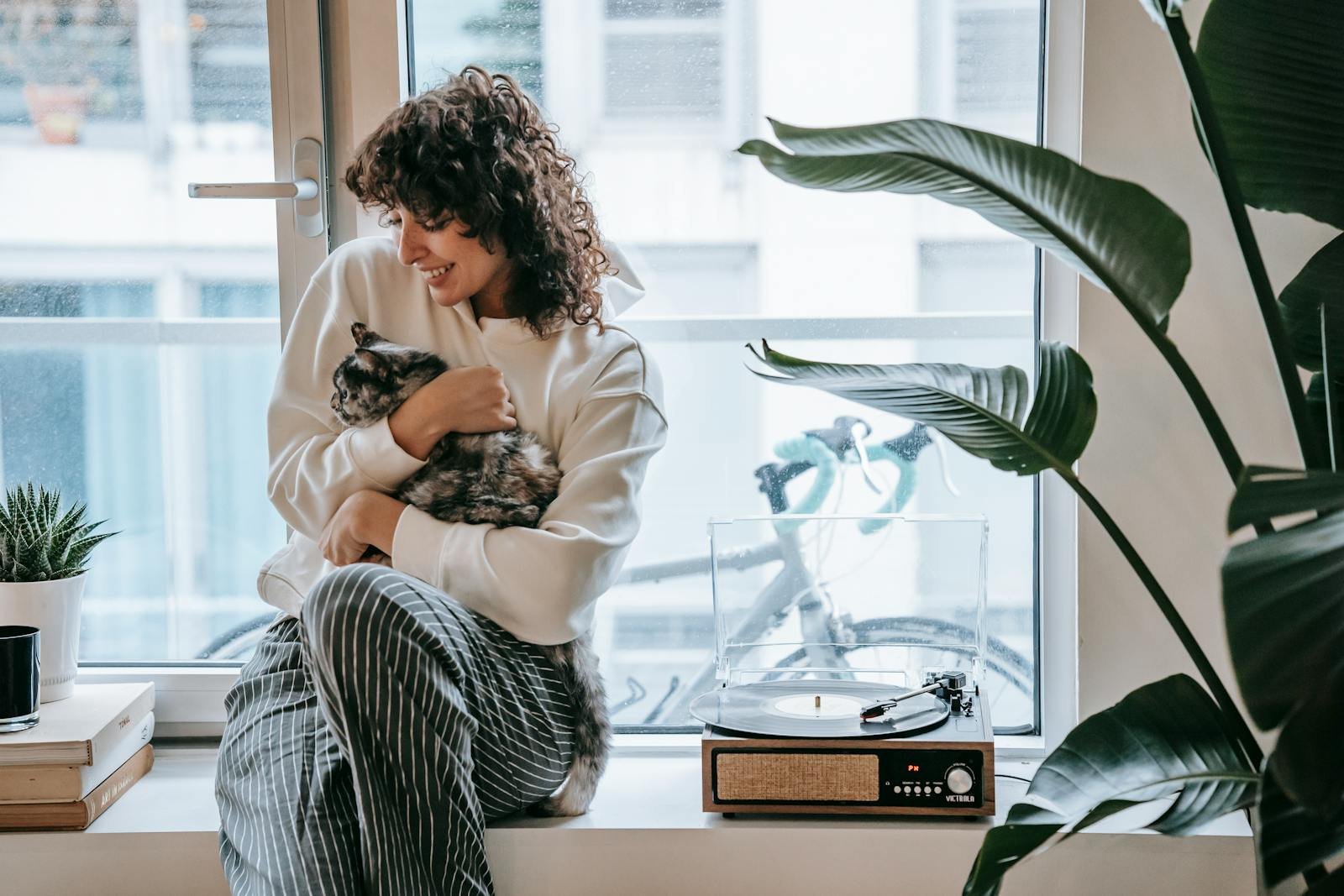 Cheerful woman with cat on window with vintage turntable