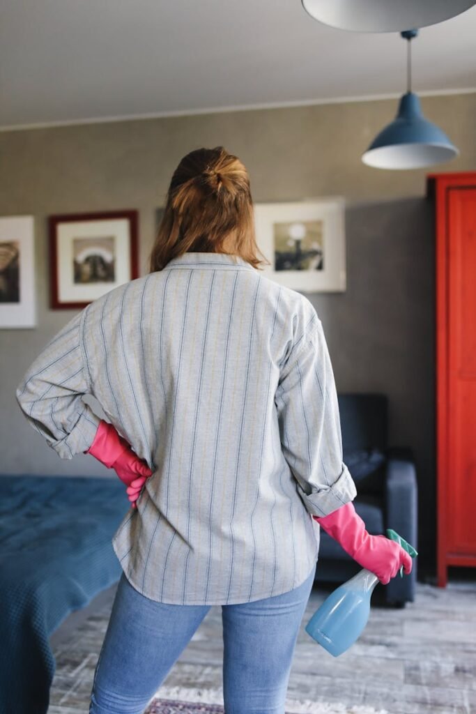 Adult woman in gloves holding a spray bottle, ready for cleaning indoors.