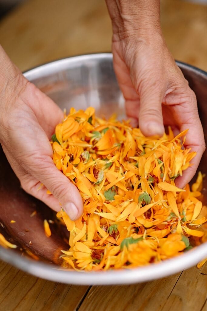 Close-up of hands mixing bright orange flower petals in a bowl, ideal for aromatherapy or natural medicine concepts.